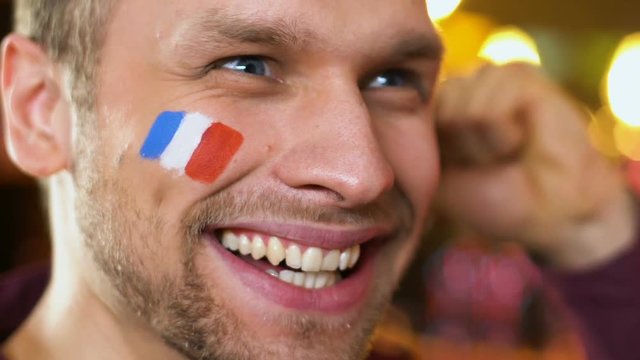 French sport fan extremely happy about favorite team winning game, flag on cheek