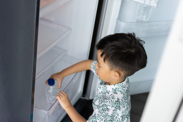 A boy is helping his mother to work at home and picking up water from fridge to his mom.