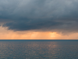 Dark clouds over calm sea at sunset