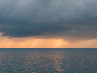 Fototapeta premium Dark clouds with sunlight over calm sea at sunset