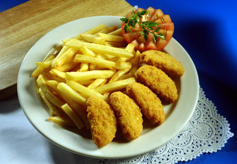 Plato de croquetas de pollo con patatas fritas y tomate.