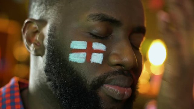 Black sports fan with English flag on cheek upset about favorite team loss
