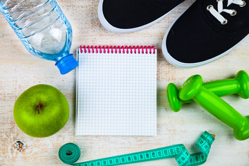 Gym shoes, dumbbells, a bottle of water, an apple and a measuring tape