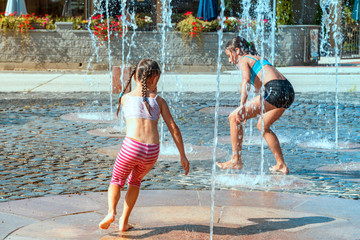Children on a sunny warm day playing outside in a water fountain. Children happily in shallow clean water on of city fountain on warm bright summer day.