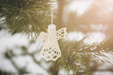 Handmade angel hanging on Christmas pine tree. Natural photo in frozen forest. Happy holidays ornaments postcard. Snowy weather.