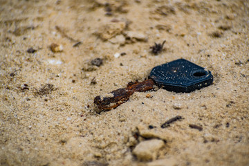 An old and rusty, lost key found in the sand on the beach. Bottle opener with black handle.