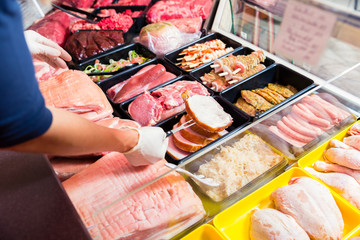 Sales woman in butcher shop putting different kinds of meat in display - Powered by Adobe