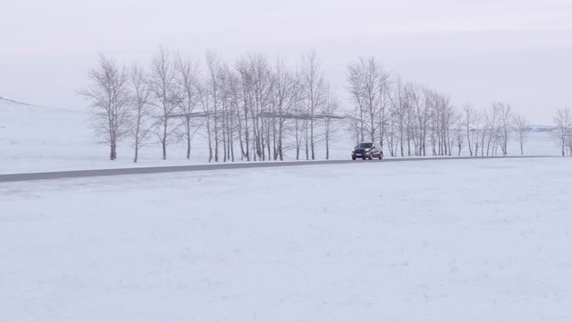 One balck crossover wagon car alone driving on highway through flat snowy field at winter evening sky - Aerial drone cinematic footage