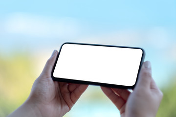 Mockup image of woman's hands holding black mobile phone with blank white screen with blurred nature background