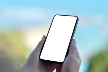 Mockup image of woman's hands holding black mobile phone with blank white screen with blurred nature background