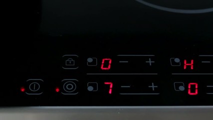 A woman presses a finger, including and setting up an electronic digital panel of a modern electric stove before starting cooking