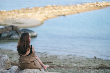 A beautiful asian woman enjoy sitting on the rock by the seashore