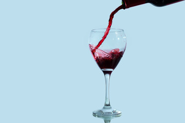 Red wine pours into a wine glass and spills, isolated against a blue background