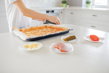 Cooking concept - cook manually adding grated cheese to pizza in the home kitchen. Close-up