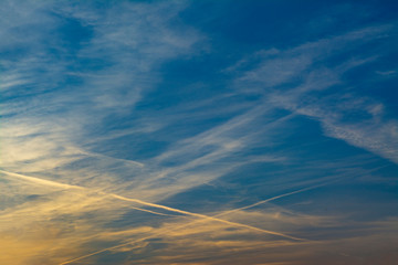 Obraz premium Clouds with jet trails from planes in the sunset sky with yellow reflections. Suitable for use as a background or cover for a book, report, presentations, slides, flyers, advertising posters.