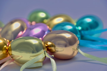 Shiny Easter eggs in various pastel shades with ribbon on a lilac background.