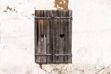 Wooden grey shutters with heart on old wall. Old wooden windows frame on stone wall.