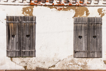 Wooden grey shutters with heart on old wall. Old wooden windows frame on stone wall.