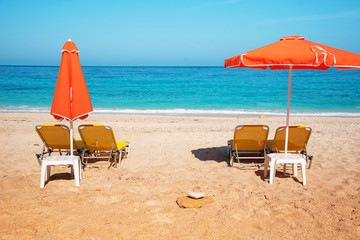 Abstract image with sun loungers and orange umbrellas from the sun on the beach on the seafront with waves (relaxation, harmony, holidays - concept)