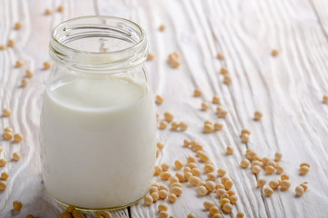 Obraz na płótnie Canvas Non-dairy alternative Soy milk or yogurt in mason jar on white wooden table with soybeans aside
