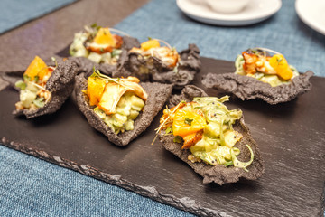Black chips of cuttlefish ink with quinoa, avocado and smoked eel filling on a flat plate at the restaurant. The concept of snacks and appetizers in haute cuisine