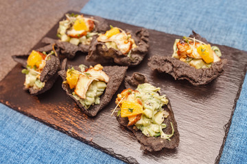 Black chips of cuttlefish ink with quinoa, avocado and smoked eel filling on a flat plate at the restaurant. The concept of snacks and appetizers in haute cuisine