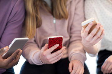 Close Up Of Three Teenage Friends Sharing Content On Mobile Phones