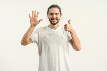 Fototapeta premium Young man with a beard shows six, five fingers and one thumb up, the number 6.