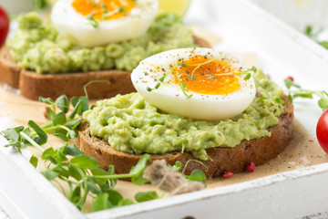 Toast with avocado puree and soft-boiled egg on white tray, liquid yolk, delicious breakfast, light sandwich. Healthy food