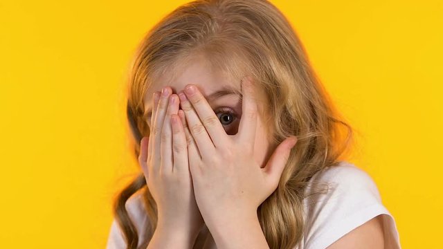 Little scared girl closing face with hands and peeking through fingers, phobia