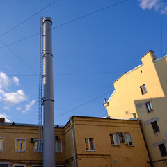 modern exhaust pipe in an old residential area with low-rise buildings against a clean blue sky. Light gray color. Stairs. Against the blue sky. Ecologically safe. Heating plant.