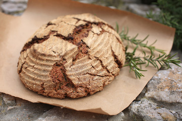Bio whole grain homemade bread made on sour dough laying on kraft paper on stone curb near rosemary, shot in rustic style.