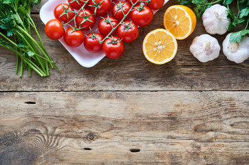 Ripe cherry tomatoes with fresh herbs, garlic and lemon on wooden background