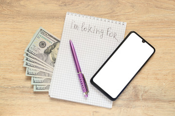 Notepad with the inscription I'm looking for  and US dollars with   smartphone  modern frame less design with isolated blank screen  on the background of a desk