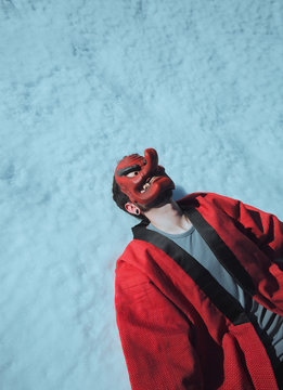 chico con mascara tengu tumbado en la nieve vestido de rojo con ropa tradicional jap&oacute;n