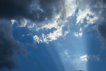 Beautiful sun rays shining through storm clouds remainings on blue sky.