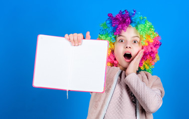 Using her imagination. Little girl in colorful hair wig with surprised face and bright imagination holding open book. Books and childrens imagination. Free play of imagination, copy space