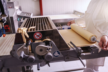 Hardworking baker in white uniform making pie crusts on machine in bakery.
