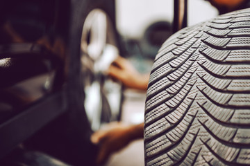 Close up of auto mechanic changing tire while crouching at workshop. Selective focus on tire.