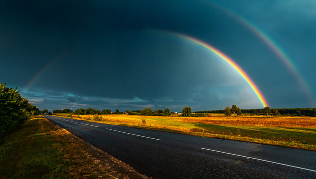 Double rainbow over the highway in darkly blue sky after a rain