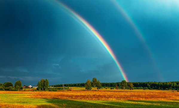 Double rainbow over the field, on which cows are grazed, in darkly blue sky after a rain - Powered by Adobe