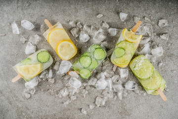 Healthy diet summer dessert, Vegan trendy ice cream. Sweet and sour infused water popsicles with cucumber, lime and lemon slices, Grey stone background copy space