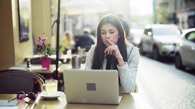 Young business woman with laptop sitting in a cafe in city, working. Slow motion.