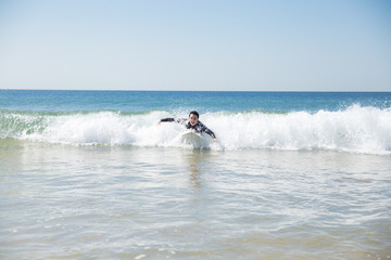 Happy young man swimming on surf board in ocean