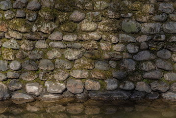Old stone wall covered with moss, reflected in the water - a beautiful vintage background