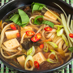 Japanese vegan soup with noodles, tofu and vegetables in a bowl, top view, close-up