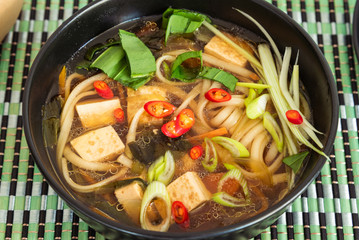 Japanese vegan soup with noodles, tofu and vegetables in a bowl, top view, close-up