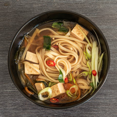 Japanese vegan soup with noodles, tofu and vegetables in a bowl, top view, close-up