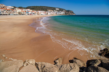 soft waves with white foam and rocks in the foreground, in the background the village of Sesimbra