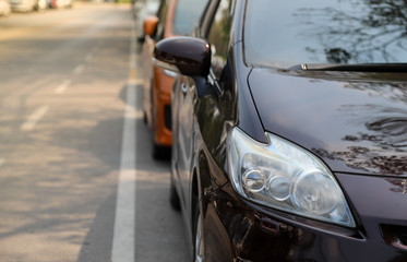 Closeup of front side of black car parking in parking area beside the street with natural background in sunny day. 